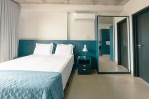 Een hotelkamer met een bed, nachtkastje, lamp, airconditioning en een spiegel.