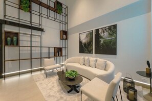 Een moderne woonkamer met een bank, fauteuils, een salontafel en een inbouwkast met planten.