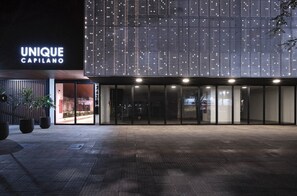 Een modern gebouw met een groot, verlicht bord waarop 'UNIQUE CAPILANO' staat en een ruime entree.