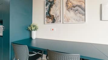 A modern dining area with a dark teal table and two perforated chairs. There are two abstract paintings on the wall above the table.