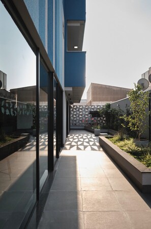 Een modern gebouw met een glazen gevel, een hekwerk met een geometrisch patroon en een pad naar een poort.