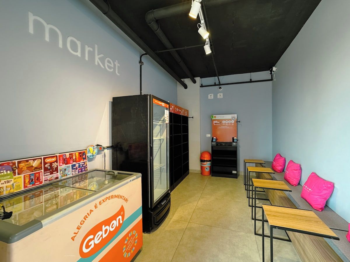 Quarto com bancada de mercado, geladeira e área de estar com almofadas cor-de-rosa.