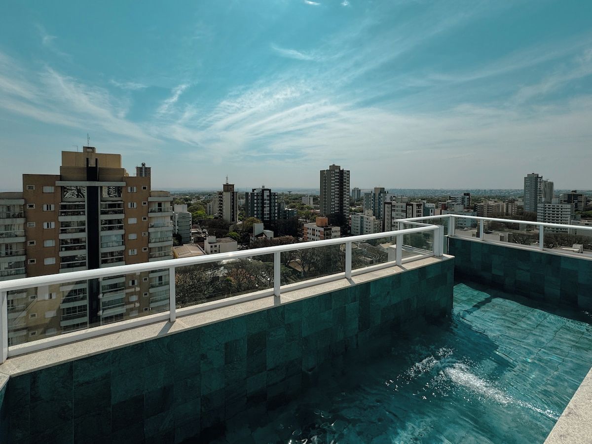 A rooftop swimming pool with a cityscape view, surrounded by high-rise buildings.