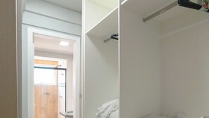 Um closet amplo com prateleiras e gavetas brancas, uma barra para pendurar roupas e um banheiro visível com vaso sanitário e chuveiro.
