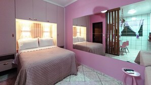 Quarto com cama, mesas de cabeceira, espelho e uma pequena mesa com um livro.