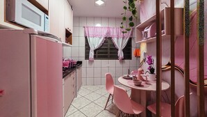 Cozinha equipada com micro-ondas, frigorífico e cadeiras cor-de-rosa à volta de uma mesa.