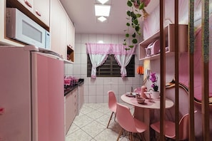 A kitchen with a microwave, refrigerator, and pink chairs around a table. - Studio Rosa Tematico Zona 7 - Perto da UEM - RJ2-04 (Maringá)