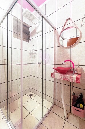 A bathroom with a glass-enclosed shower, a pink sink, and a mirror. - Studio Rosa Tematico Zona 7 - Perto da UEM - RJ2-04 (Maringá)
