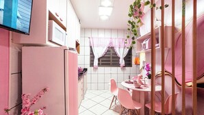 Cozinha com área de refeições, paredes com azulejos brancos, geladeira, micro-ondas e cadeiras cor de rosa.