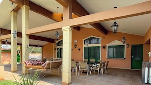 Um pátio externo com cadeira de balanço, mesa de jantar, cadeiras e uma porta verde.