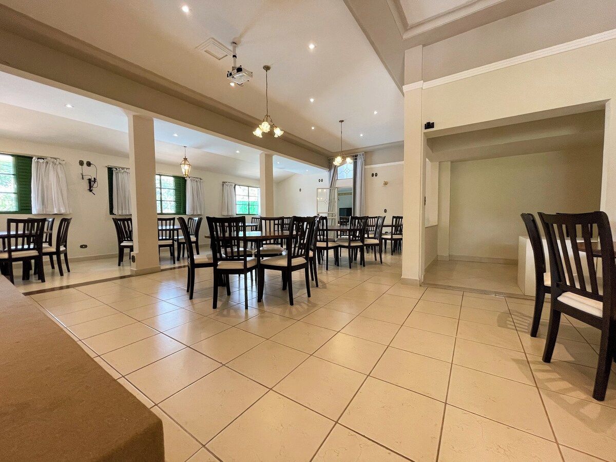 A spacious dining area with multiple tables and chairs, a projector, and ceiling lights.
