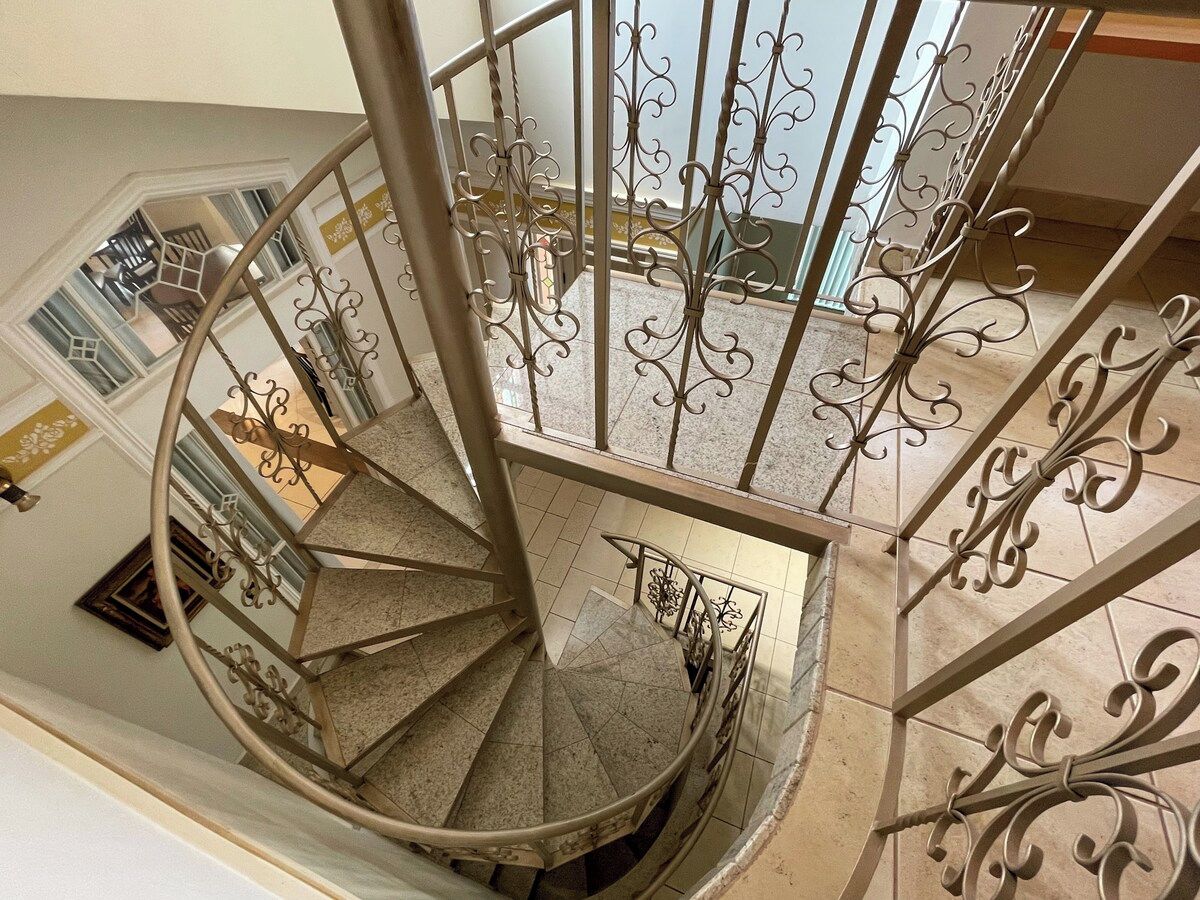 A spiral staircase with ornate metal railings and a view of the upper floor.