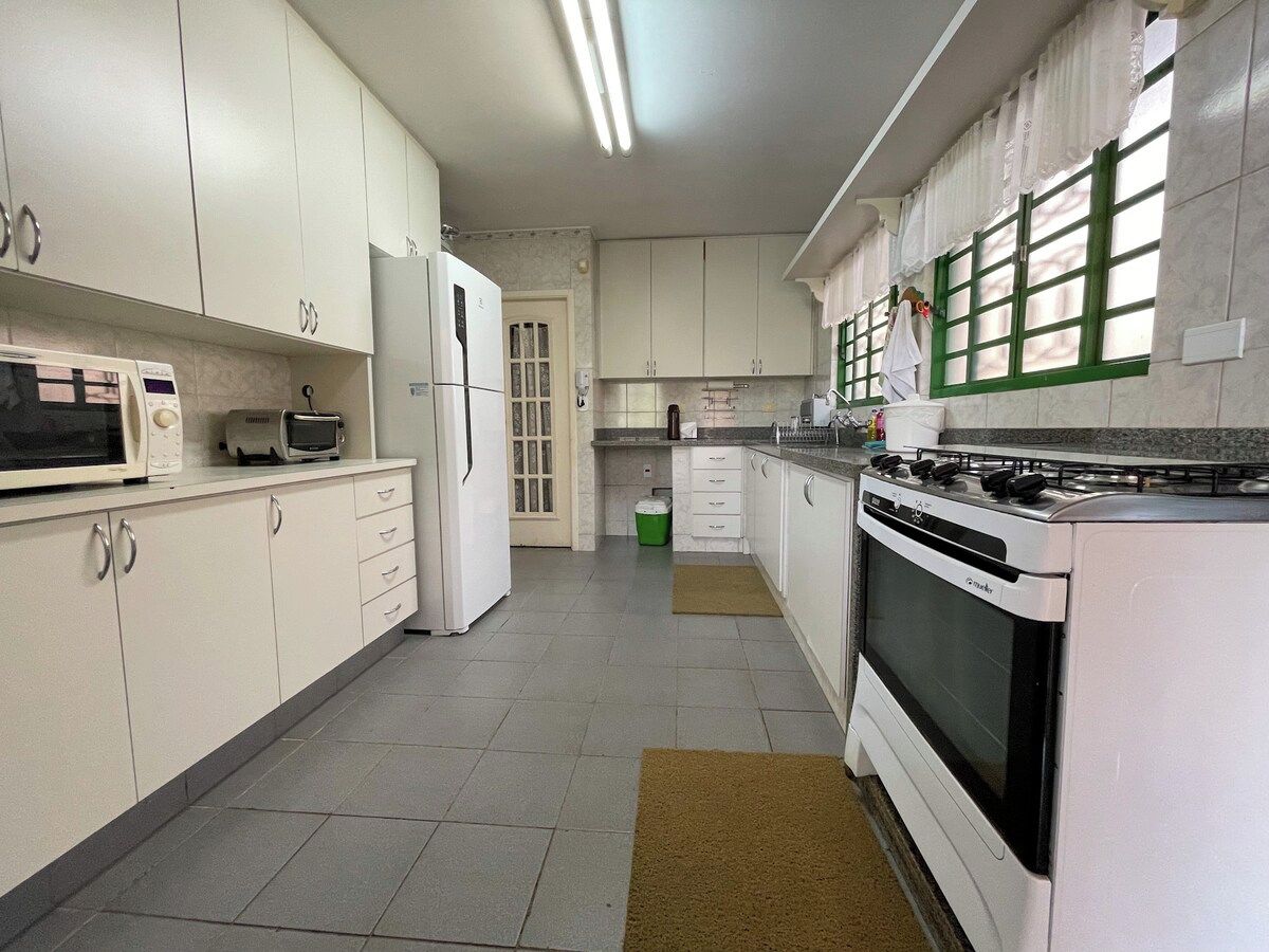A kitchen with white cabinets, a microwave, a toaster, a stove, and a green trash bin.