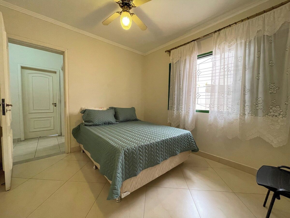 A bedroom with a bed, a ceiling fan, a window with curtains, and a door.
