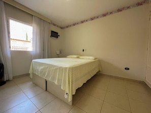 Ein Schlafzimmer mit einem Bett, Vorhängen, einer Wandklimaanlage und einem gefliesten Boden.