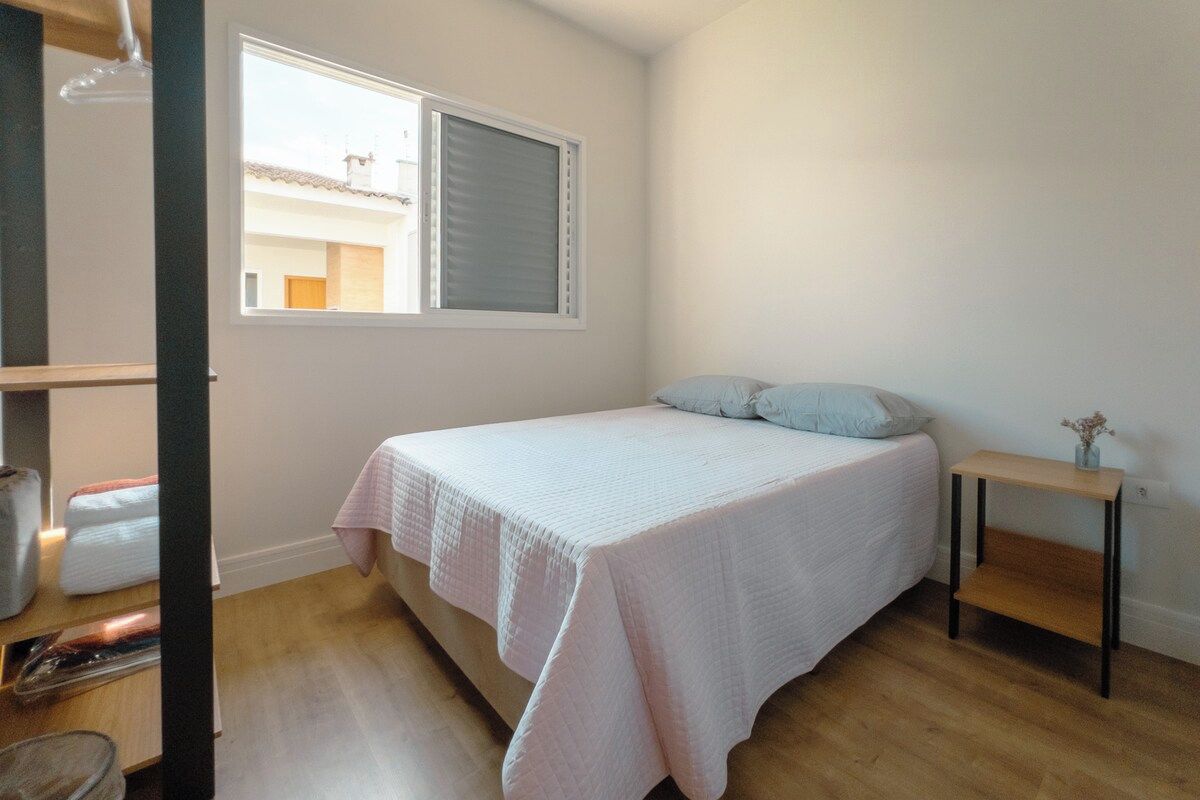 Quarto com cama, janela, mesa de cabeceira e cadeira.
