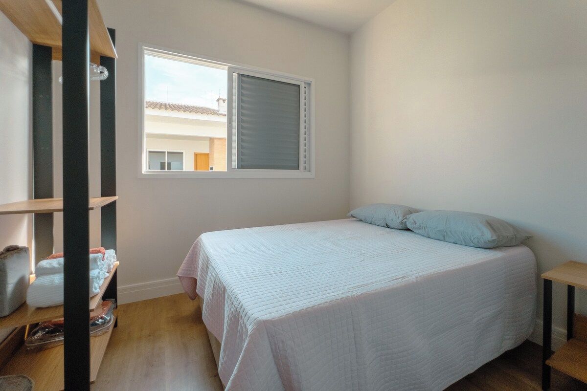 A bedroom with a bed, a window, and a shelf with folded towels.