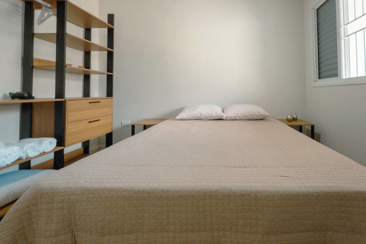 A single bed with a quilted cover, a wooden nightstand with a lamp, and a built-in shelf unit with storage drawers.
