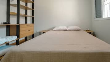 A single bed with a quilted cover, a wooden nightstand with a lamp, and a built-in shelf unit with storage drawers.