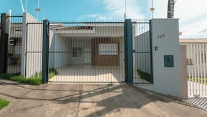 Uma entrada fechada por portão, com um caminho de concreto que leva a um edifício com a placa de número 705.