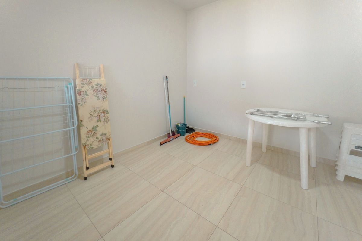 Una habitación con un perchero metálico, una escalera de madera, un trapeador, una escoba y una mesa con una silla.