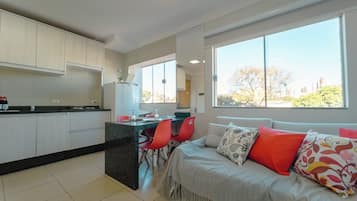 A modern kitchen with white cabinets, a dining area with red chairs, and a large window with a view of trees and buildings.