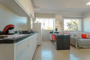 A modern kitchen with white cabinets, a red kettle, and a dining area with a sofa and chairs. - Zona 7 Apartment with AC and Wi-Fi - MN204 (Maringá)