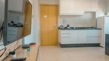 A compact kitchen with a wooden door, a flat-screen TV, and a small countertop with a coffee maker.