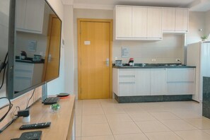 A compact kitchen with a wooden door, a flat-screen TV, and a small countertop with a coffee maker.