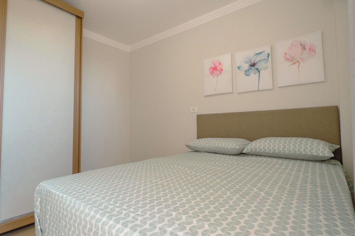 Quarto com cama, almofadas e três quadros de flores na parede.
