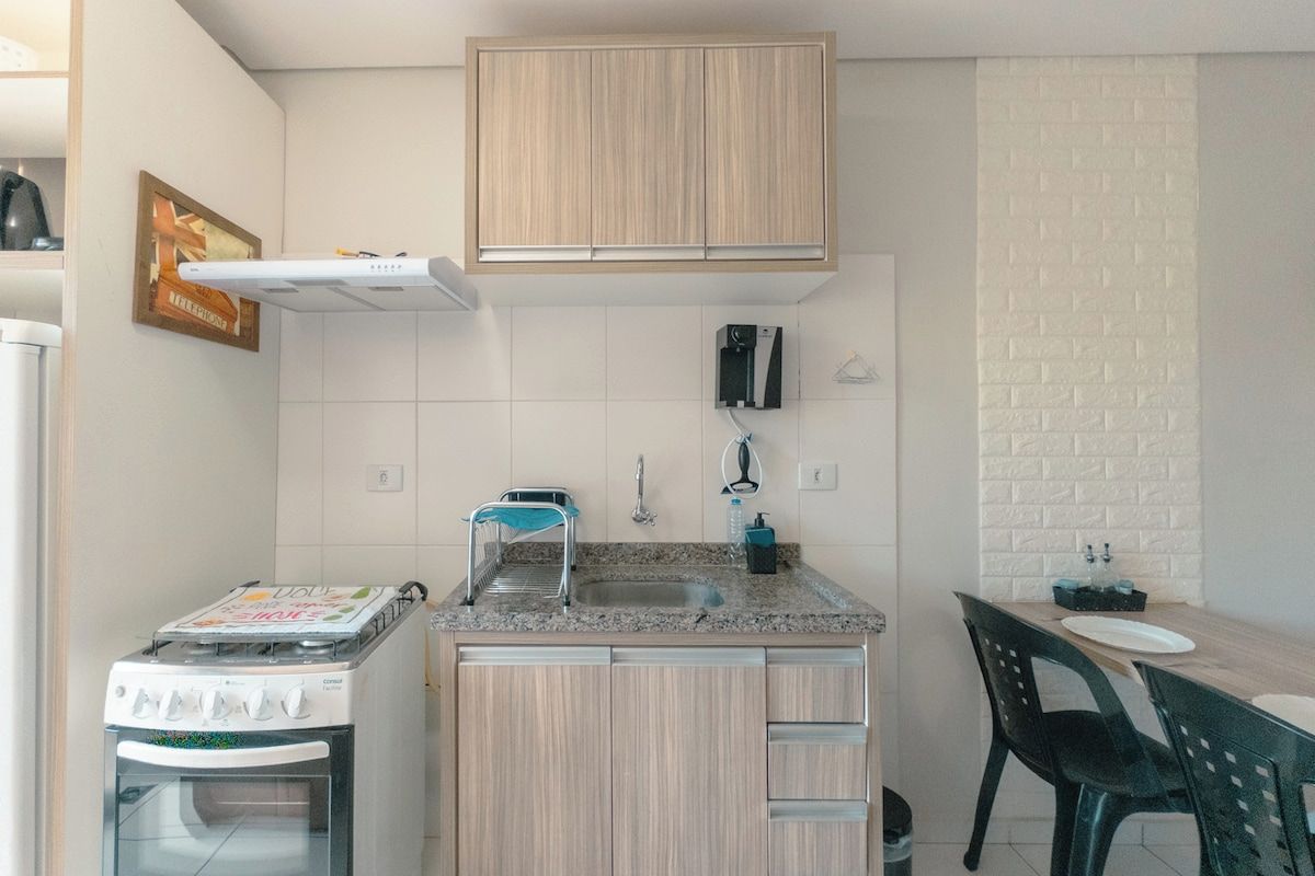 Una cocina compacta con horno integrado, un lavamanos y una zona de comedor con mesa y sillas.