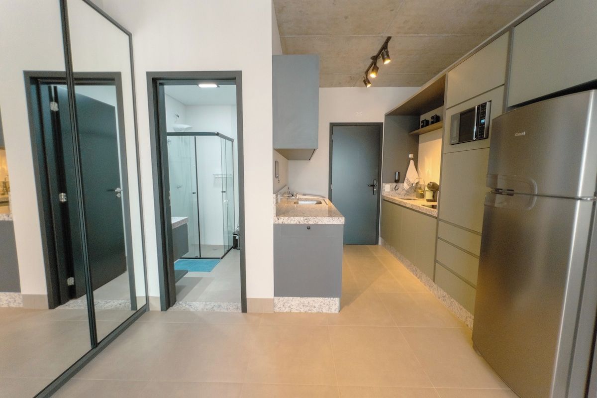 Una cocina moderna con electrodomésticos de acero inoxidable, encimera gris y puerta de cristal que da a un baño.