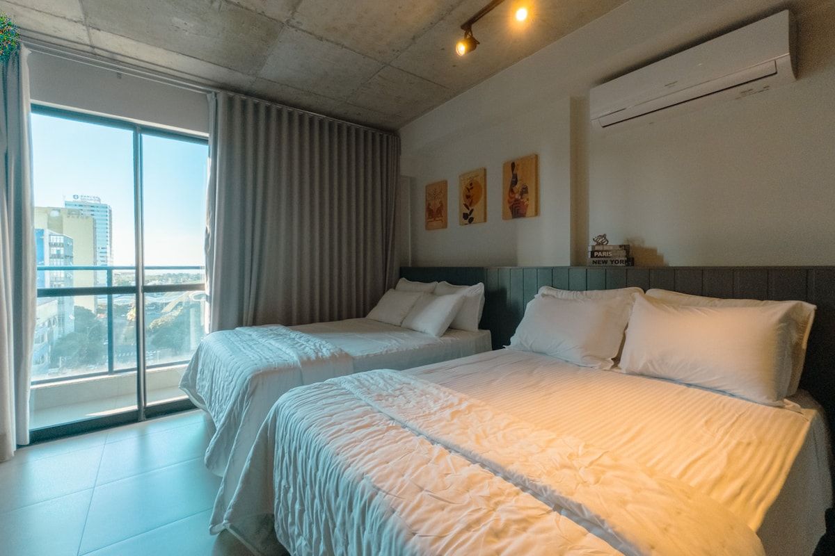 Ein Hotelzimmer mit zwei Betten, einem großen Fenster und Blick auf die Stadt.