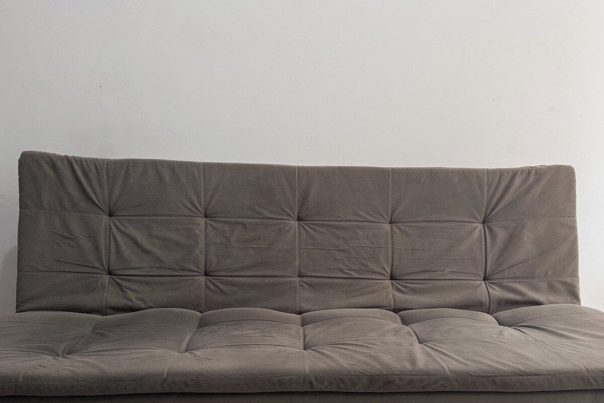 Un sofá tapizado gris con respaldo capitonado y asiento acolchado.