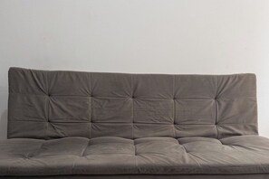 A grey upholstered sofa with a tufted backrest and cushioned seat. - Affordable Apartment with AC in Zona 7 - CED103 (Maringá)