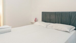 A neatly made bed with white linens and a dark headboard in a simple room with a white wall and a small nightstand with a red object. - Affordable Apartment with AC in Zona 7 - CED103 (Maringá)