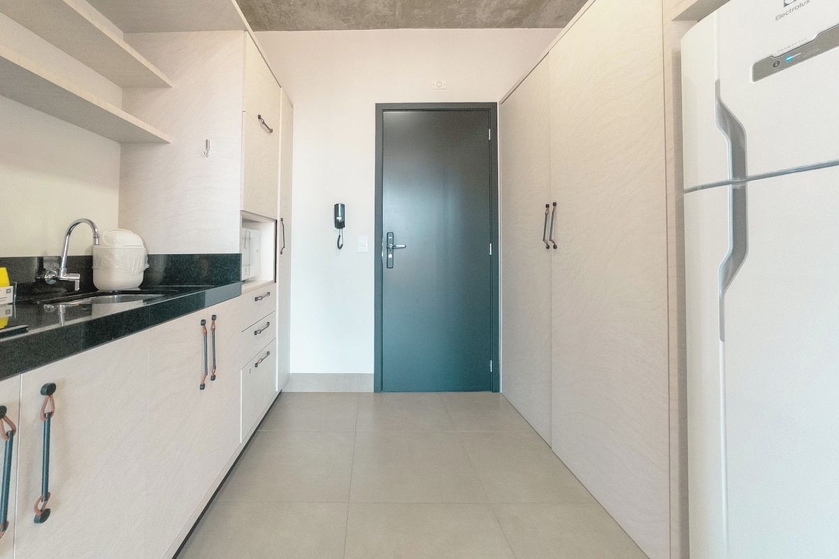 Ein schmaler Flur mit einer Tür am Ende, einem Waschbecken links und einem Kühlschrank rechts.