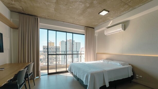 Habitación de hotel moderna con una cama grande, un escritorio y vistas a la ciudad a través de amplios ventanales.