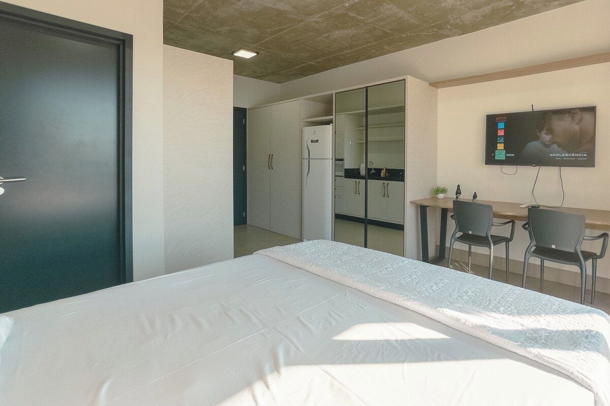 Ein Hotelzimmer mit einem Bett, einem Schreibtisch mit zwei Stühlen, einem an der Wand befestigten Fernseher und einem Kleiderschrank.