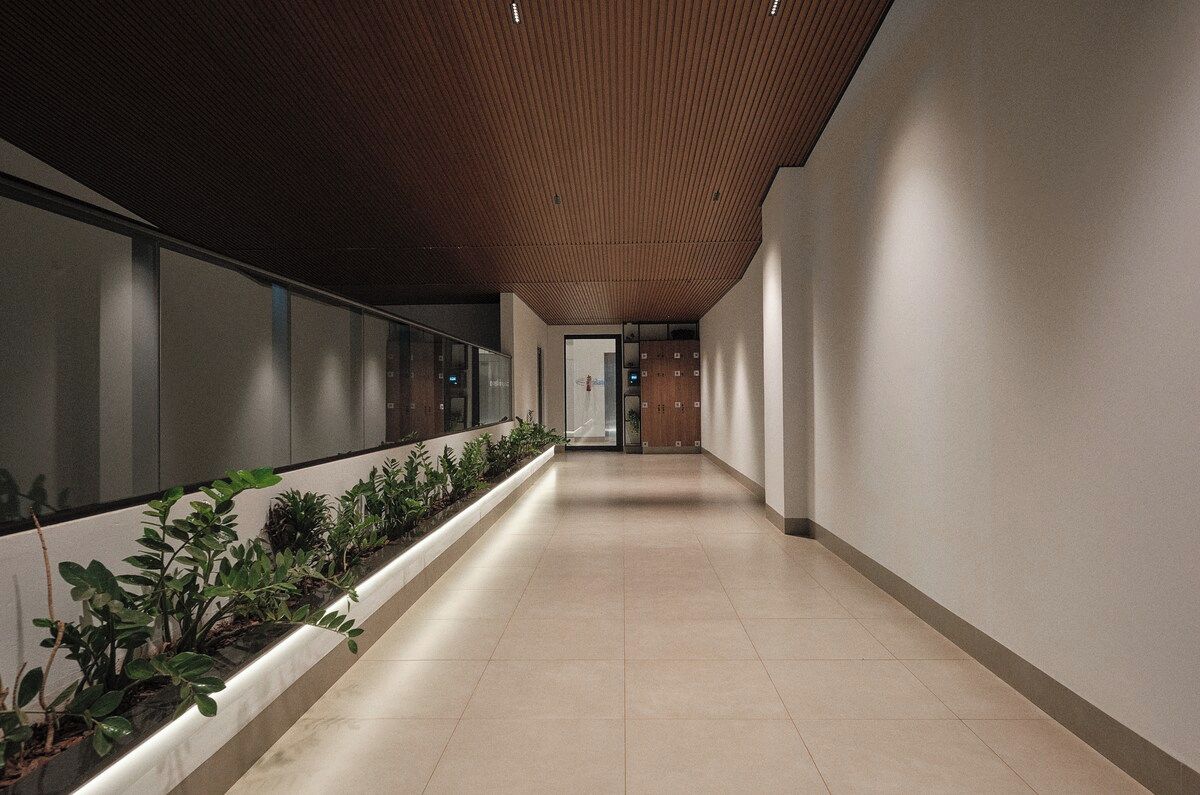 A corridor with a wooden ceiling, a plant-lined wall, and a tiled floor.
