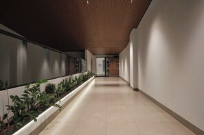 A corridor with a wooden ceiling, a plant-lined wall, and a tiled floor.
