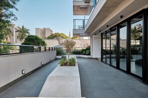 A modern building with a flat roof terrace, large windows, and a small garden area.
