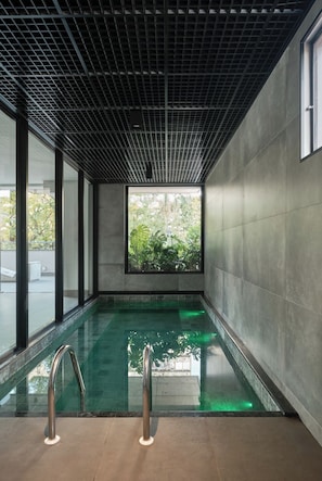 Una piscina interior moderna con techo de diseño enrejado y amplios ventanales.