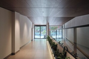 A corridor with a sloped ceiling, glass doors leading outside, and a railing with plants.