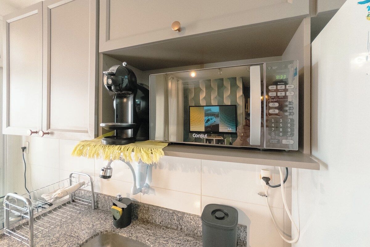 A kitchen area with a coffee machine, a digital clock, and a trash bin.