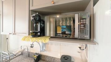 A kitchen area with a coffee machine, a digital clock, and a trash bin.