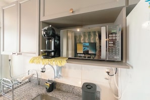 A kitchen area with a coffee machine, a digital clock, and a trash bin.