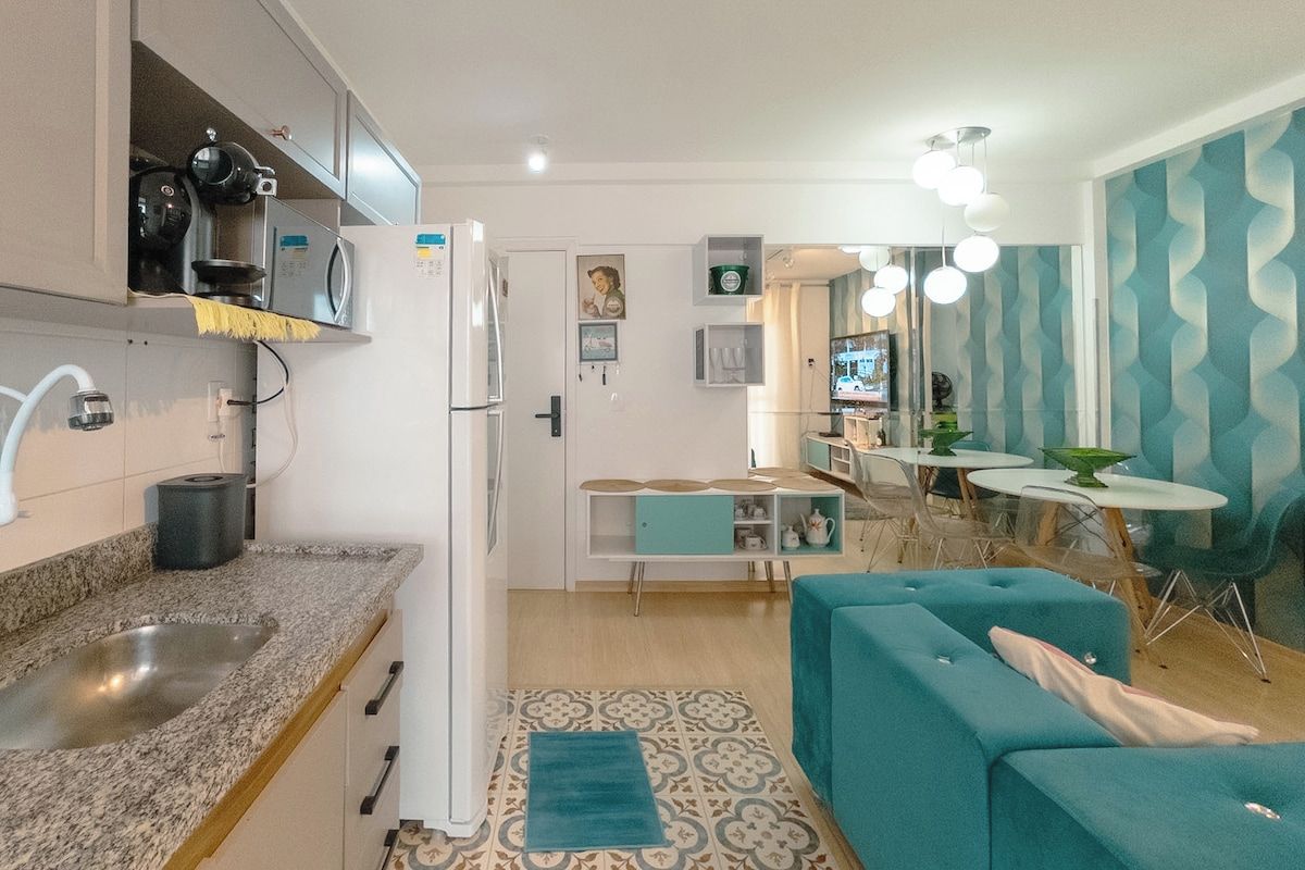A compact kitchen with a refrigerator, microwave, and stove, a dining area with a table and chairs, and a living area with a sofa and a rug.