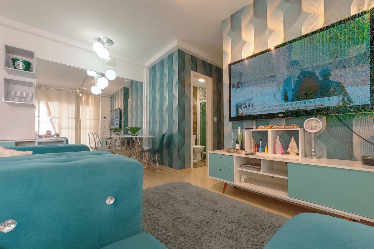 Sala de estar moderna com sofás cor turquesa, TV de tela plana e um painel decorativo na parede.