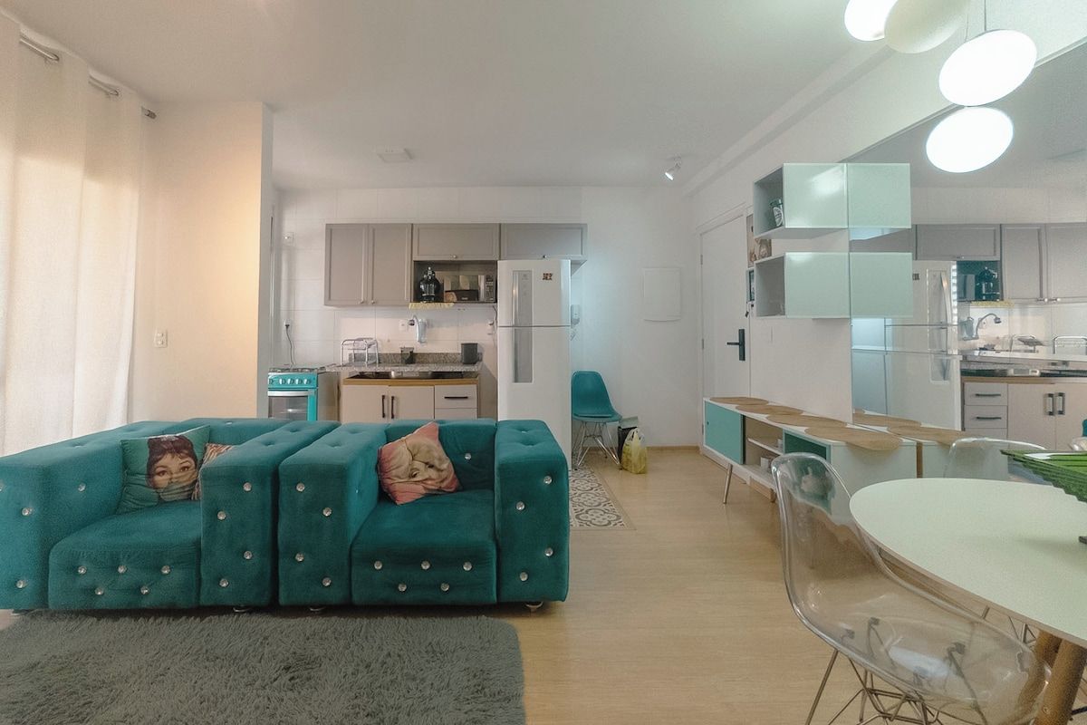 A modern apartment with a teal sofa, a dining table, and a kitchen area.